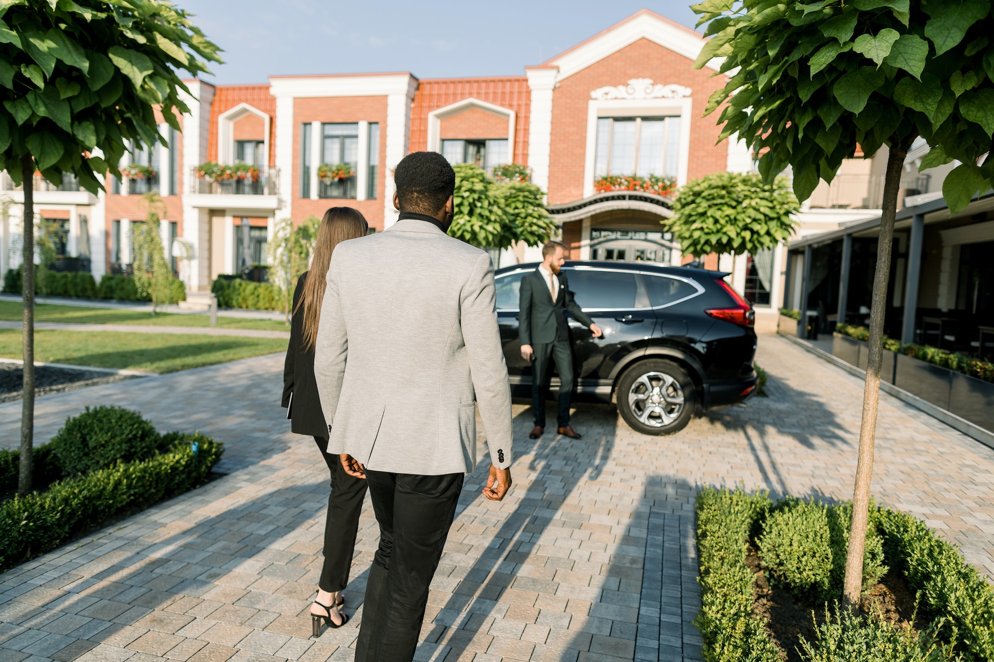 Back view of business couple, African man and Caucasian woman partners, walking to the black car on